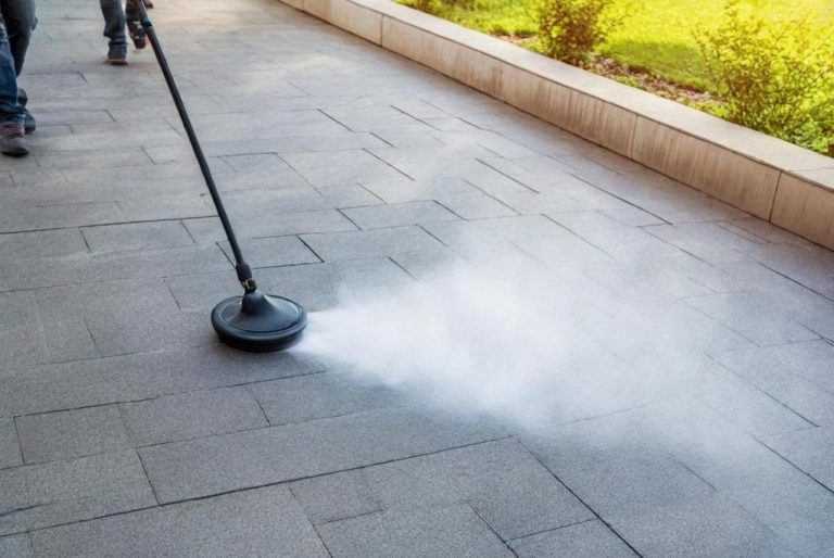 Ein Mann reinigt den Boden mit einem Hochdruckgerät, während Dampf aufsteigt.